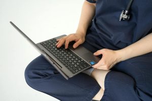 A medical professional in scrub suit using a laptop, representing remote healthcare work.