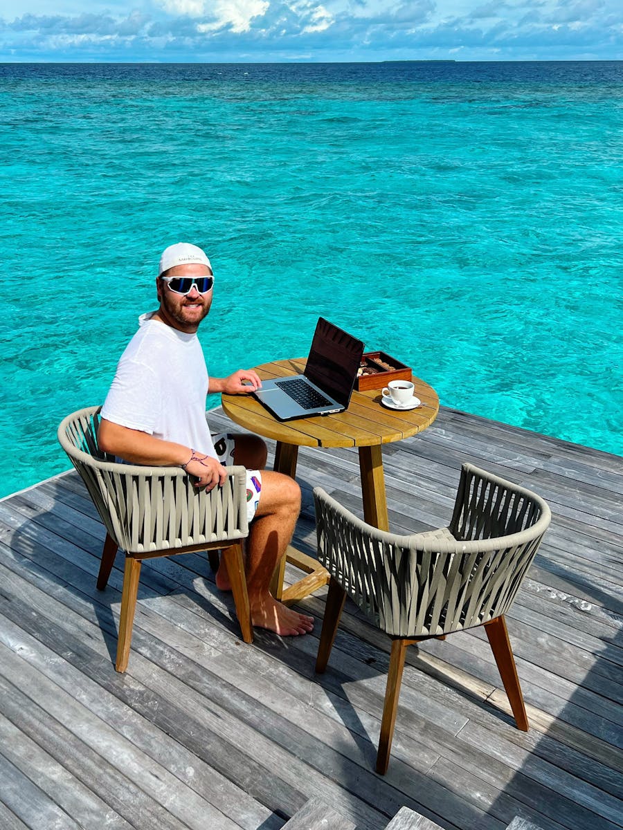 Man working on a laptop by the ocean, embodying remote work lifestyle.