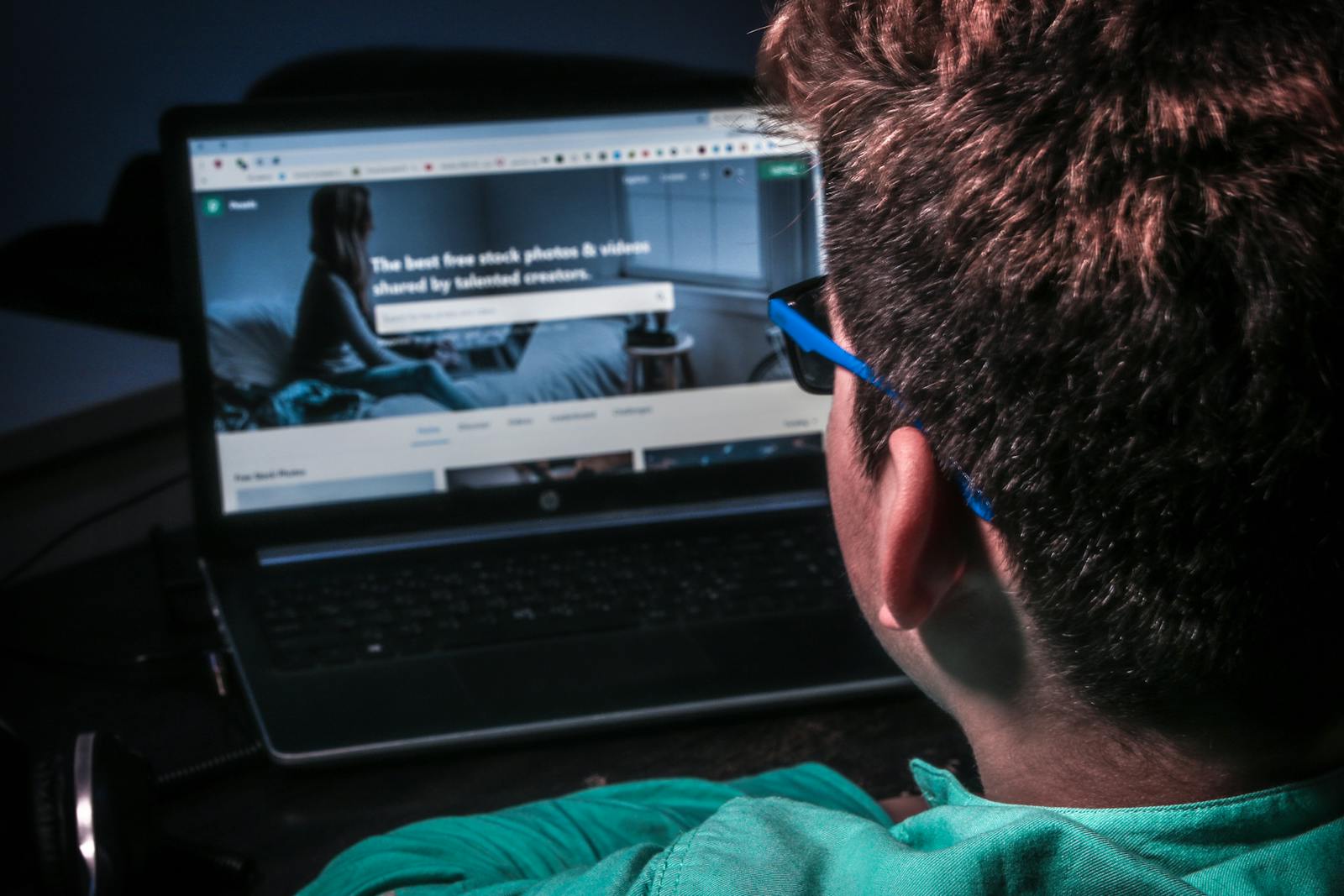 Close-up of a person using a laptop to browse stock photos online in dim lighting.