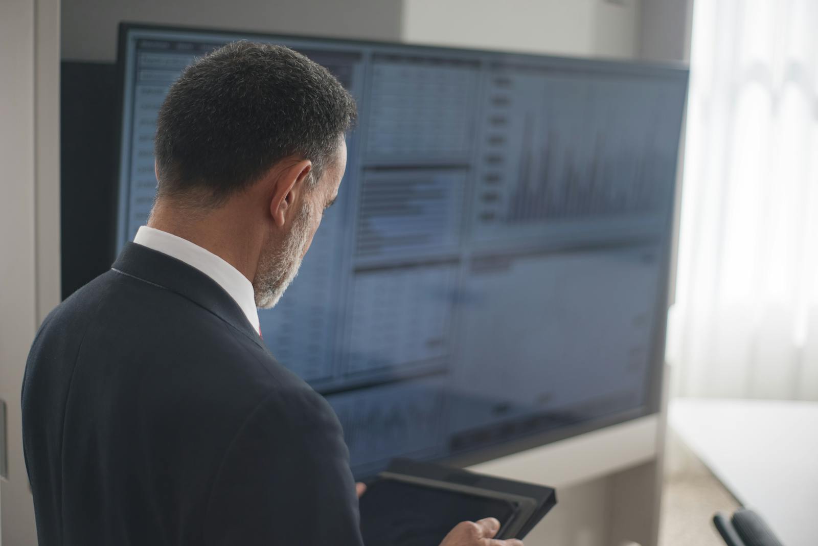 Professional analyzing stock markets on a digital tablet in a modern office setting.