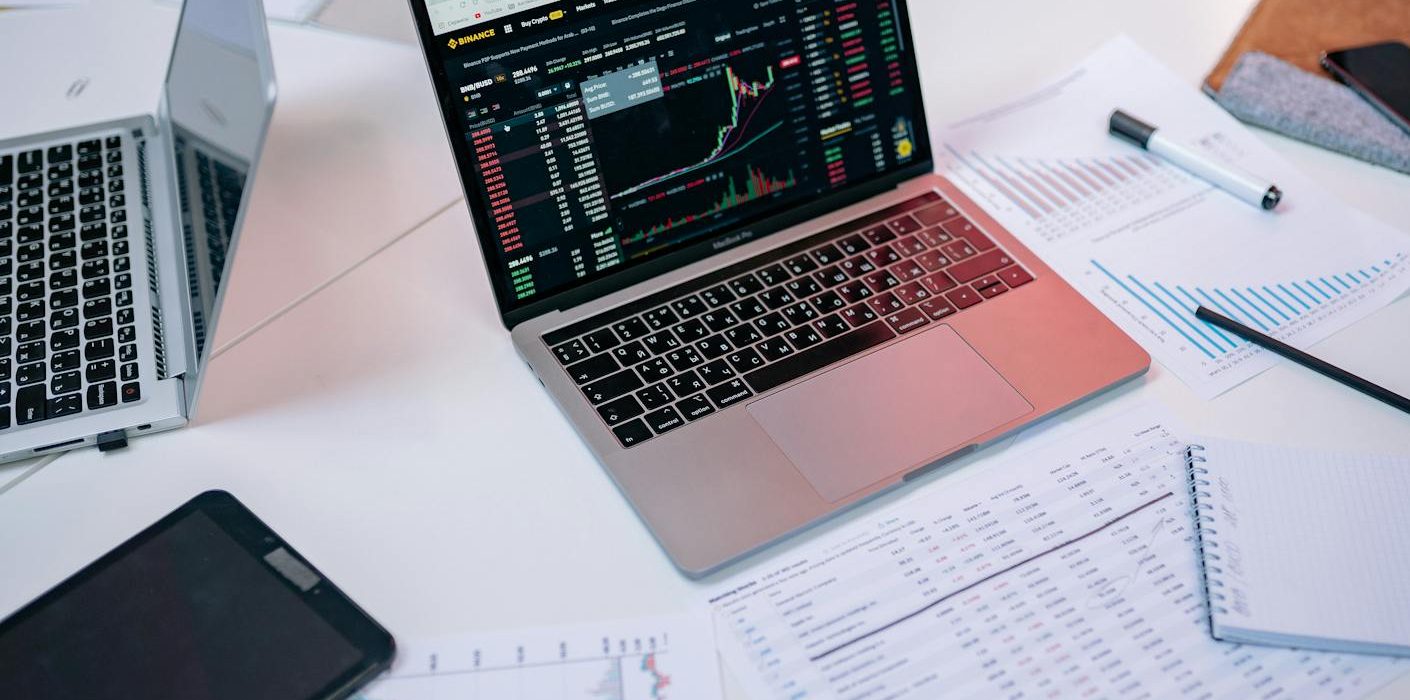 Laptops on a desk displaying stock market charts and financial documents.