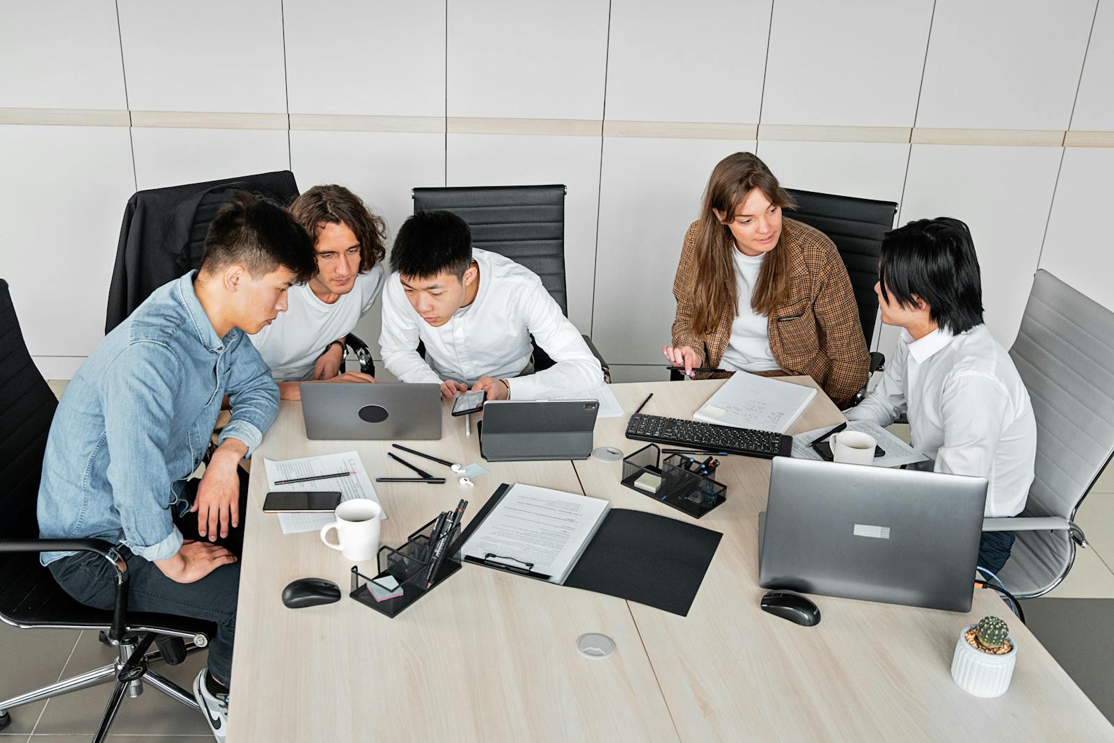 A diverse group of colleagues working together in an office setting with laptops and documents.